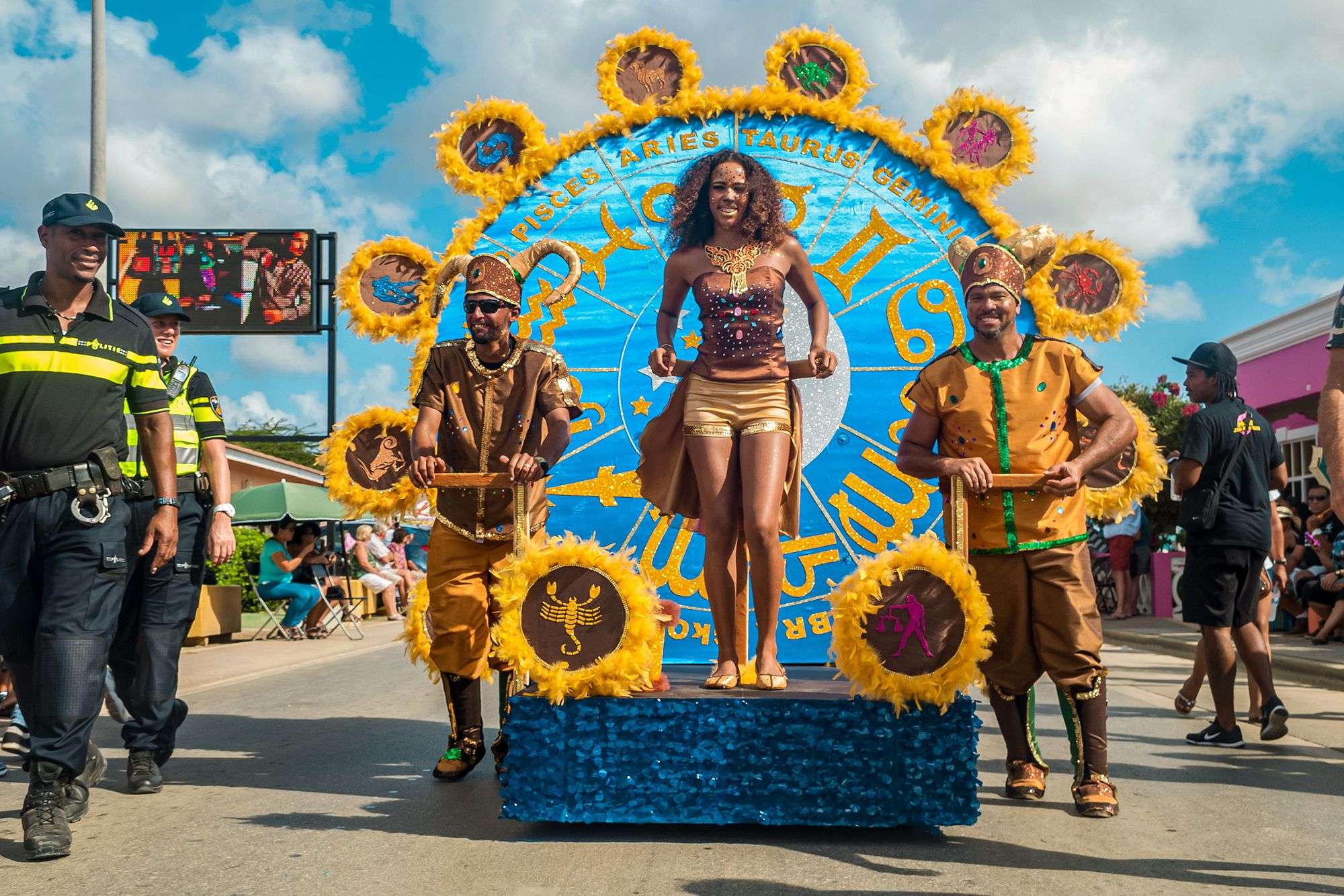 Woman and two men in costume guiding a horoscope float in a carnival parade in Curacao