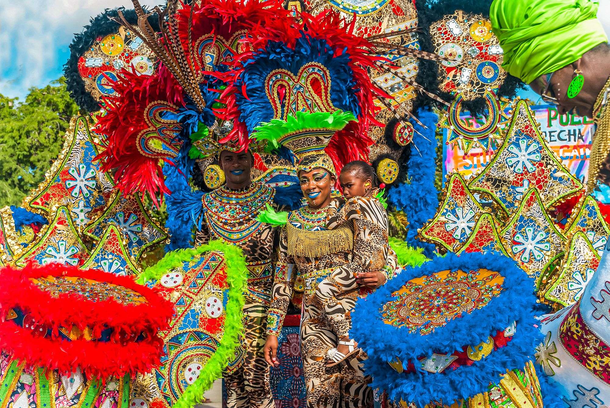 Woman in brilliantly colored costume, closely followed by a man and child in equally brilliant costumes in Curacao