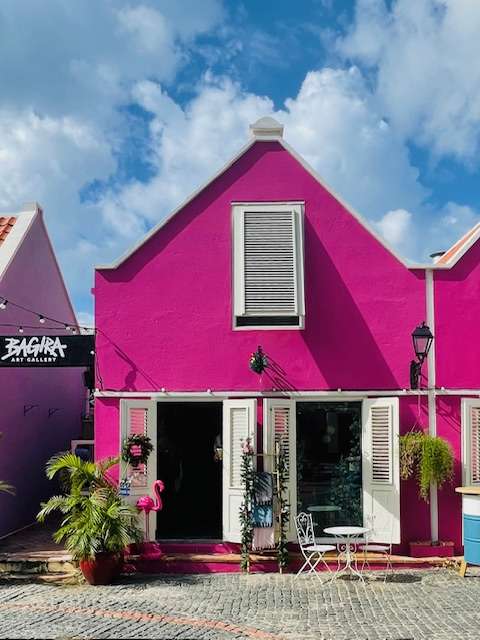 Hot pink cottage with white louvred doors and window with cafe table and chair in front in Curacao shop