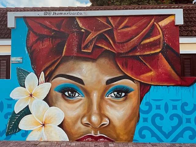 Colorful street art featuring beautiful native woman with two white tropical flowers and a red headdress in Curacao