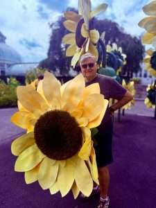 Person with large sunflower sculptures outdoors.