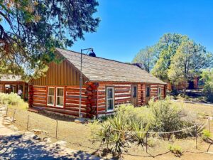 Rustic log cabin surrounded by trees and shrubs.