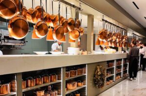 Professional kitchen with hanging copper pots and chefs.