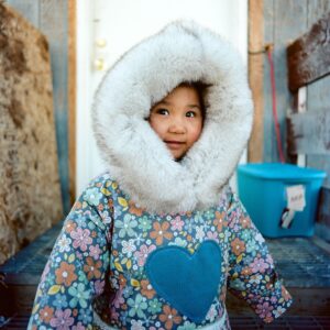 Child in fur hooded floral coat smiling at camera.