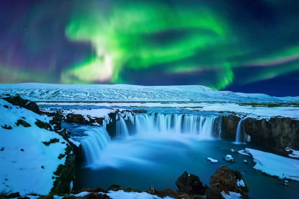 Northern lights over snowy waterfall scene
