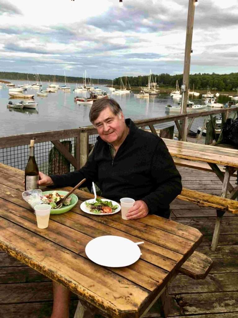 Man enjoying meal by lakeside with boats. Best Restaurants mid-Coast Maine