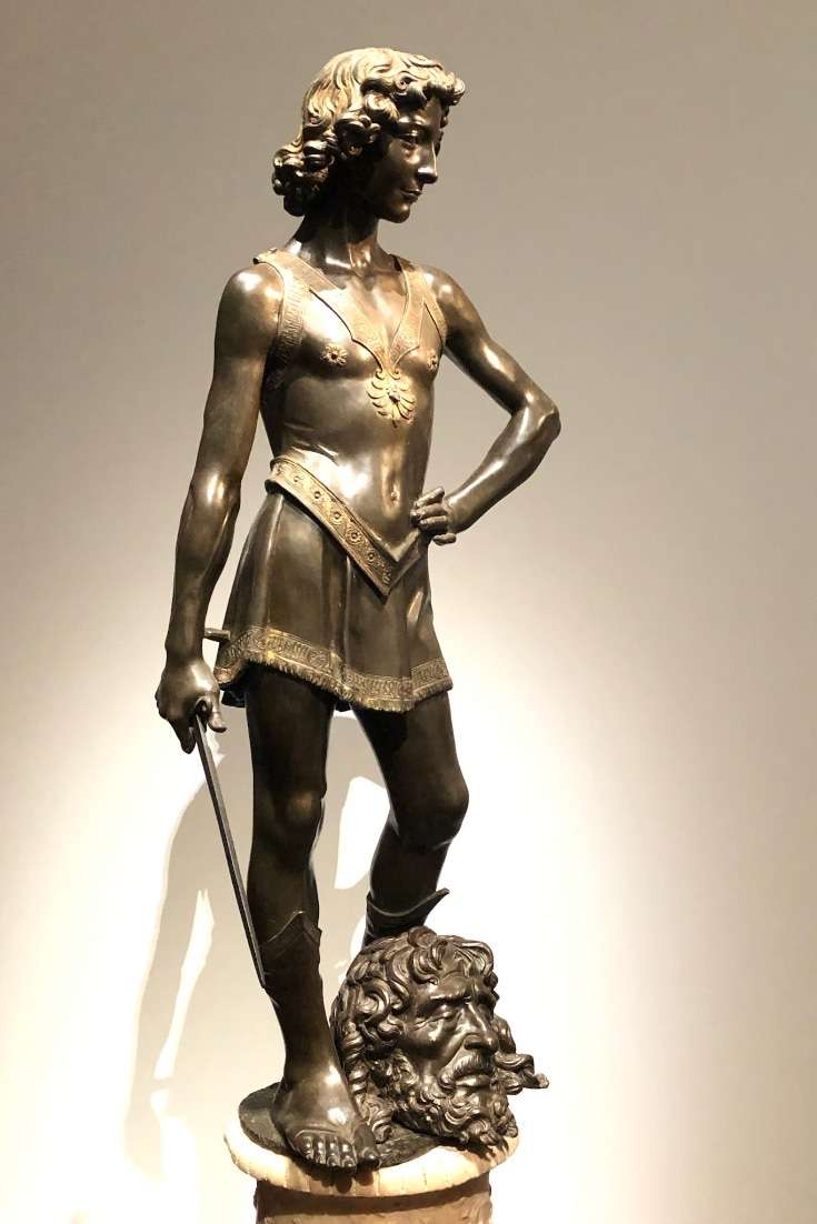 A sculpture of young David with curly hair and a head at his feet in museum in Florence