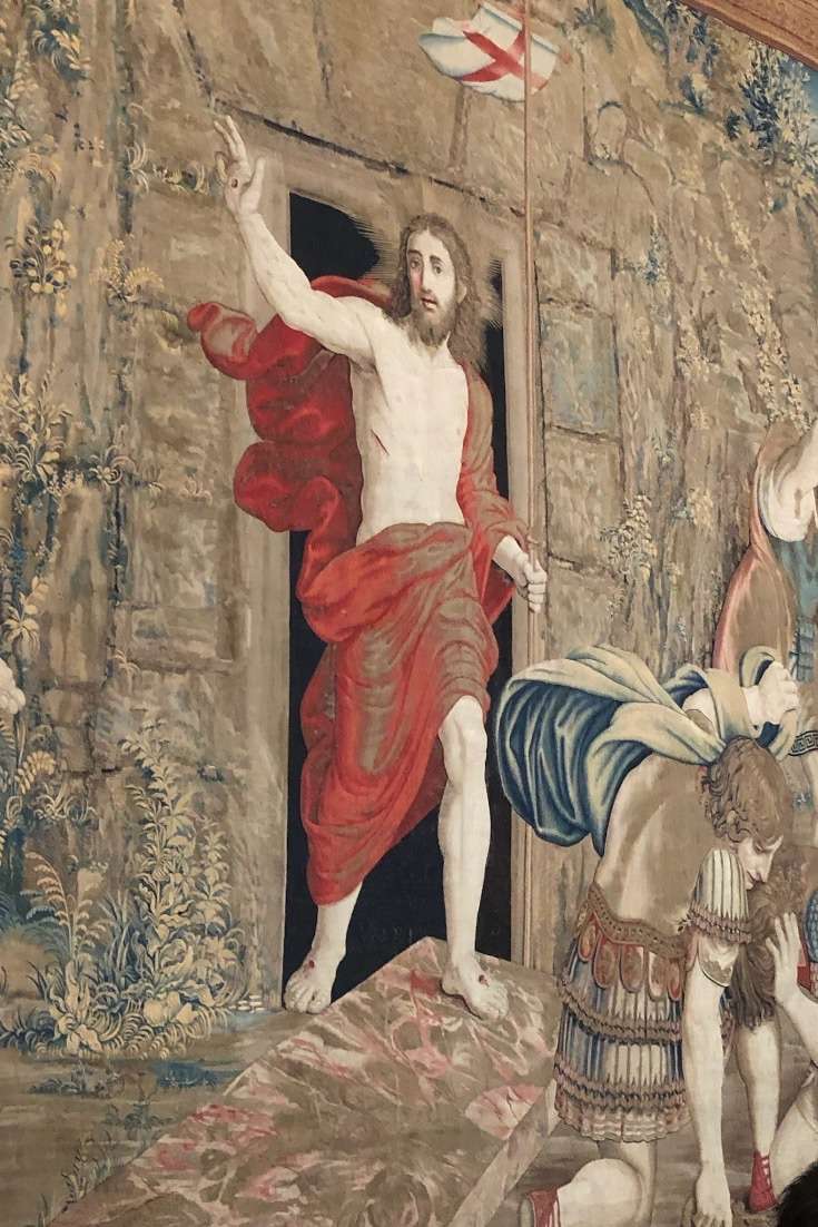 A tapestry with Christ, his right hand in the air wearing red garments in front of an opening at the Vatican Museum in Rome