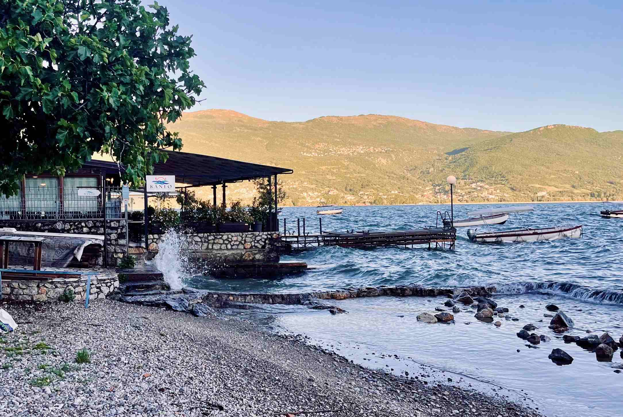 Alnania tings to do: Lake Ohrid and the Kaneo Restaurant near sunset with splashing waves, rowboats and a covered deck overlooking the lake in North Macedonia