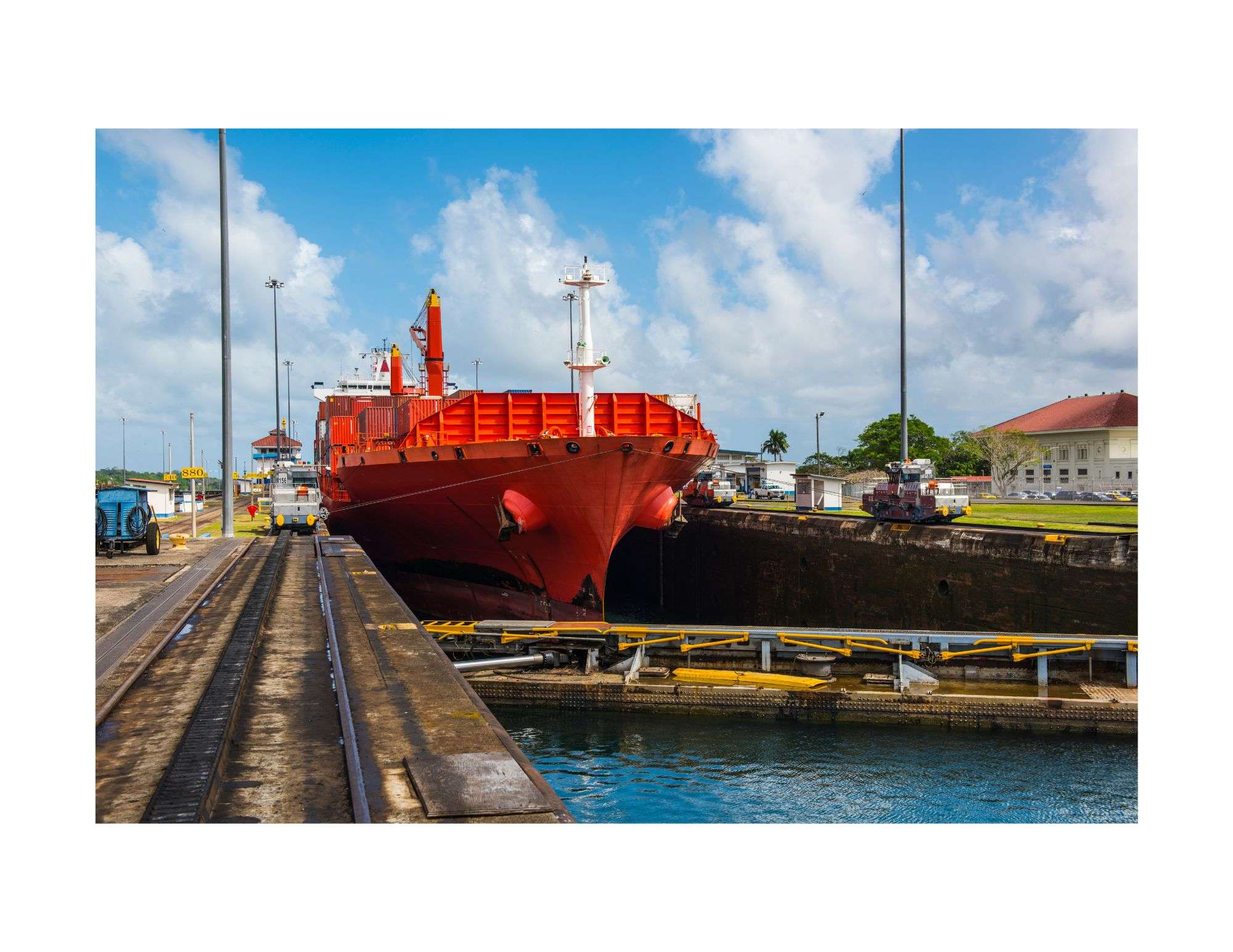 Enormous bright red ship being pulled along the Panama Canal by trains along the tracks