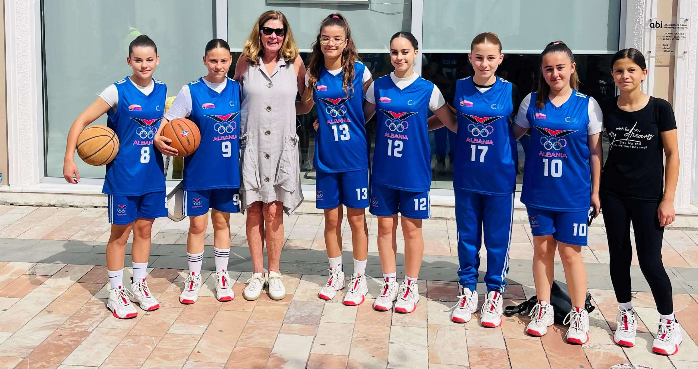 Robin with 6 girls in blue basketball uniforms and one coach in black with two basketballs in Shkoder, Albania