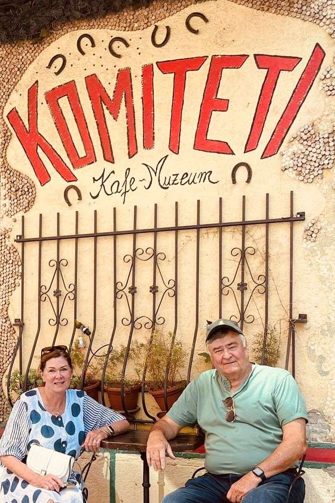 Robin and Paul sitting in front of Komiteti Kafe-Muzeum with iron wall, horseshoes and tiles in Tirana Albania