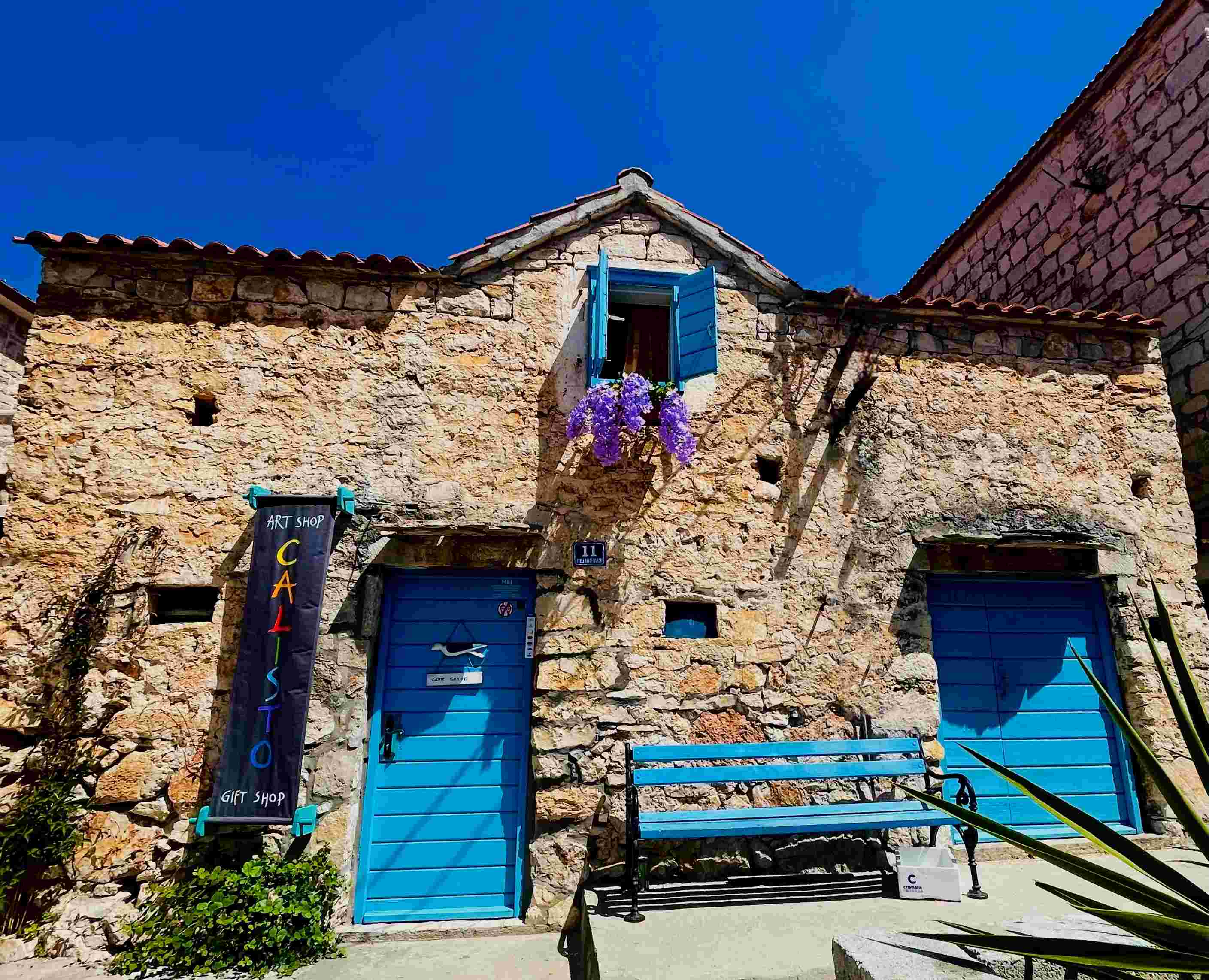 Stone house with blue shutters and purple flowers in Maslinica in Croatia