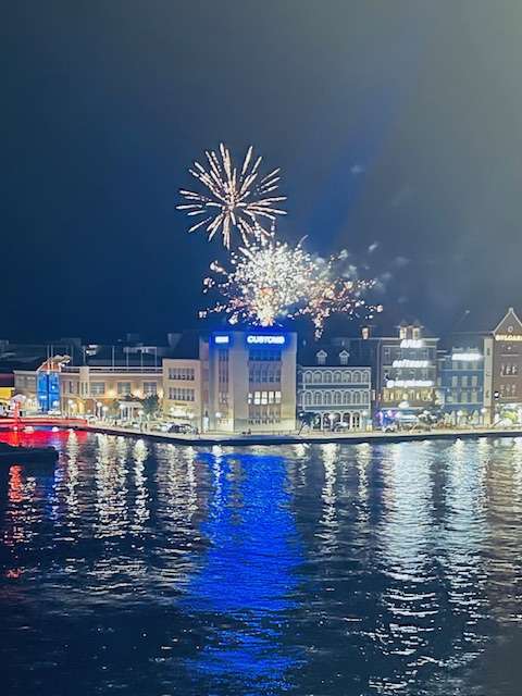 White fireworks displays over town in Curacao with reflections in the water at night