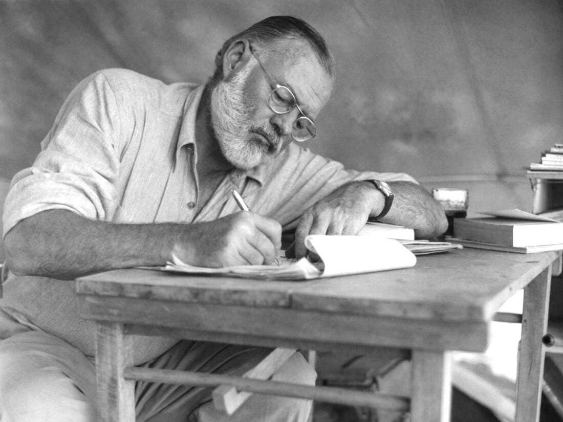 Ernest Hemingway writing in a messy pile of paper while sitting at a wooden table in Key West