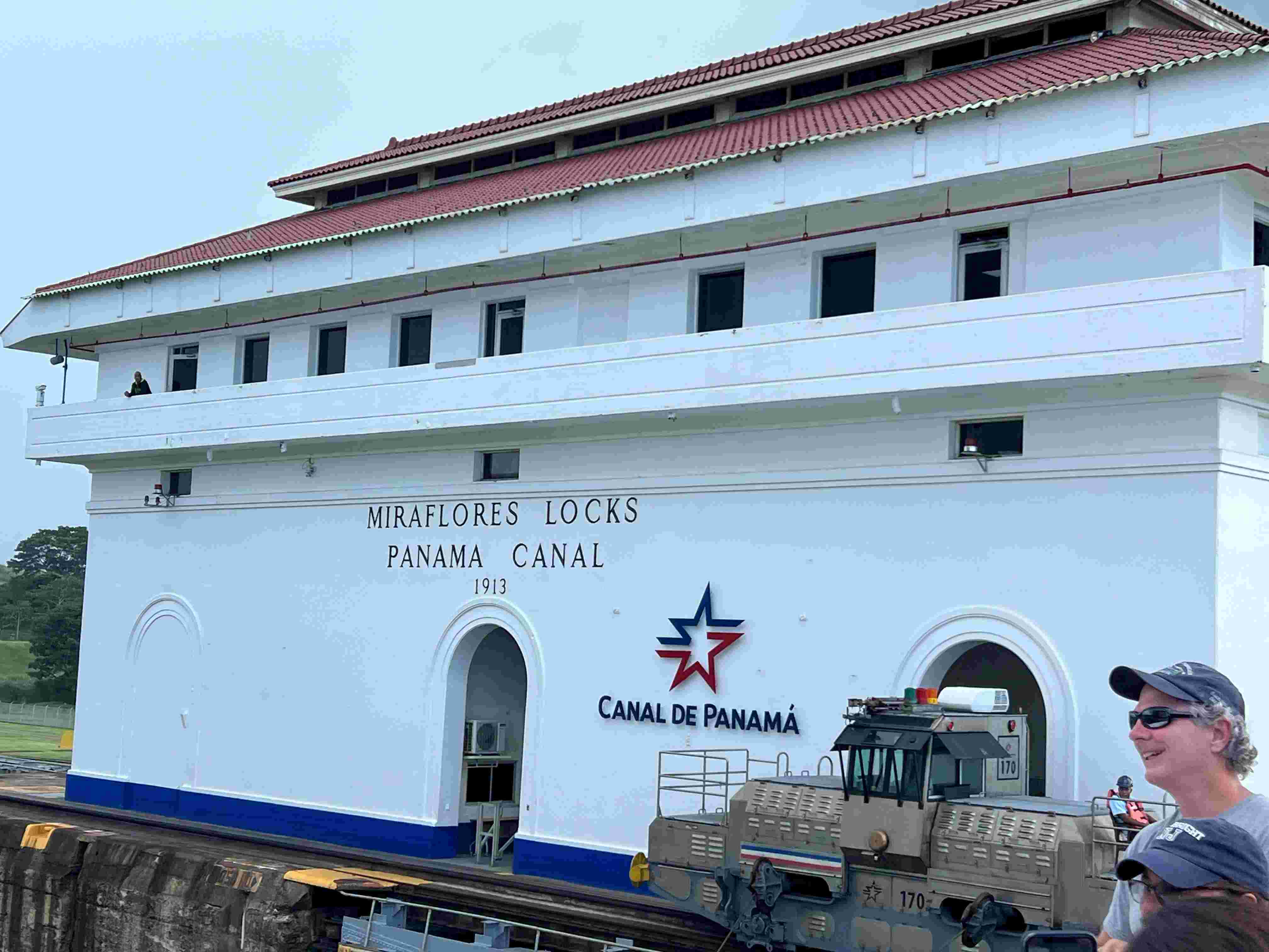 Man in baseball cap in front of the White Miraflores Locks building on the Panama Canal