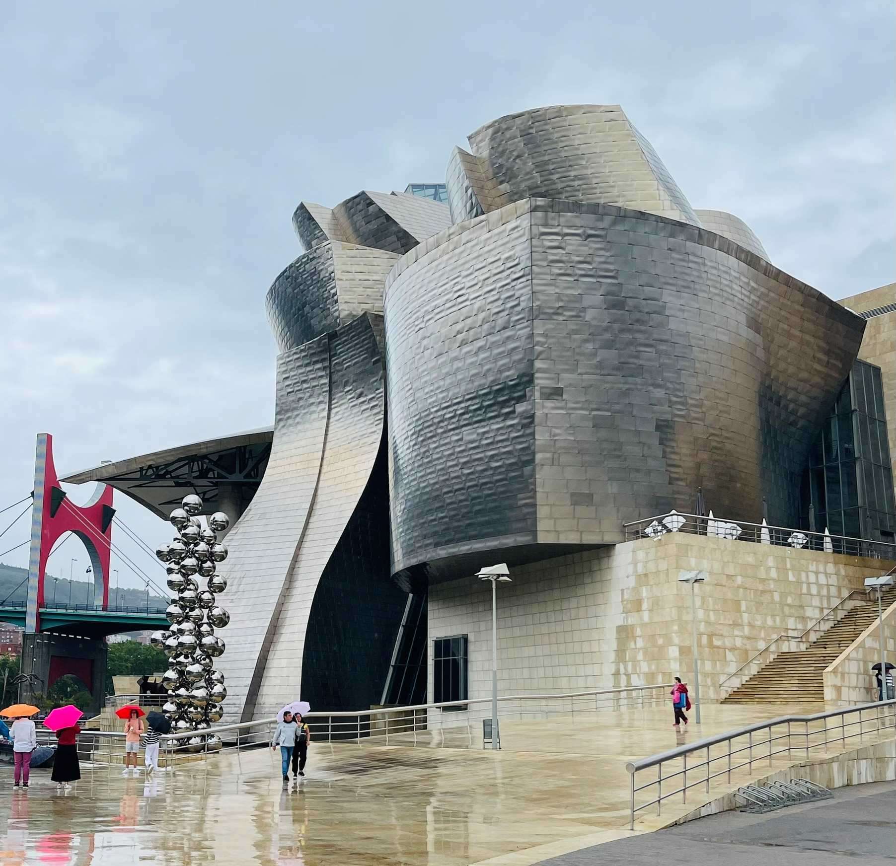 Modern silver-gray building with people carrying umbrellas at Guggenheim Museum in Bilbao