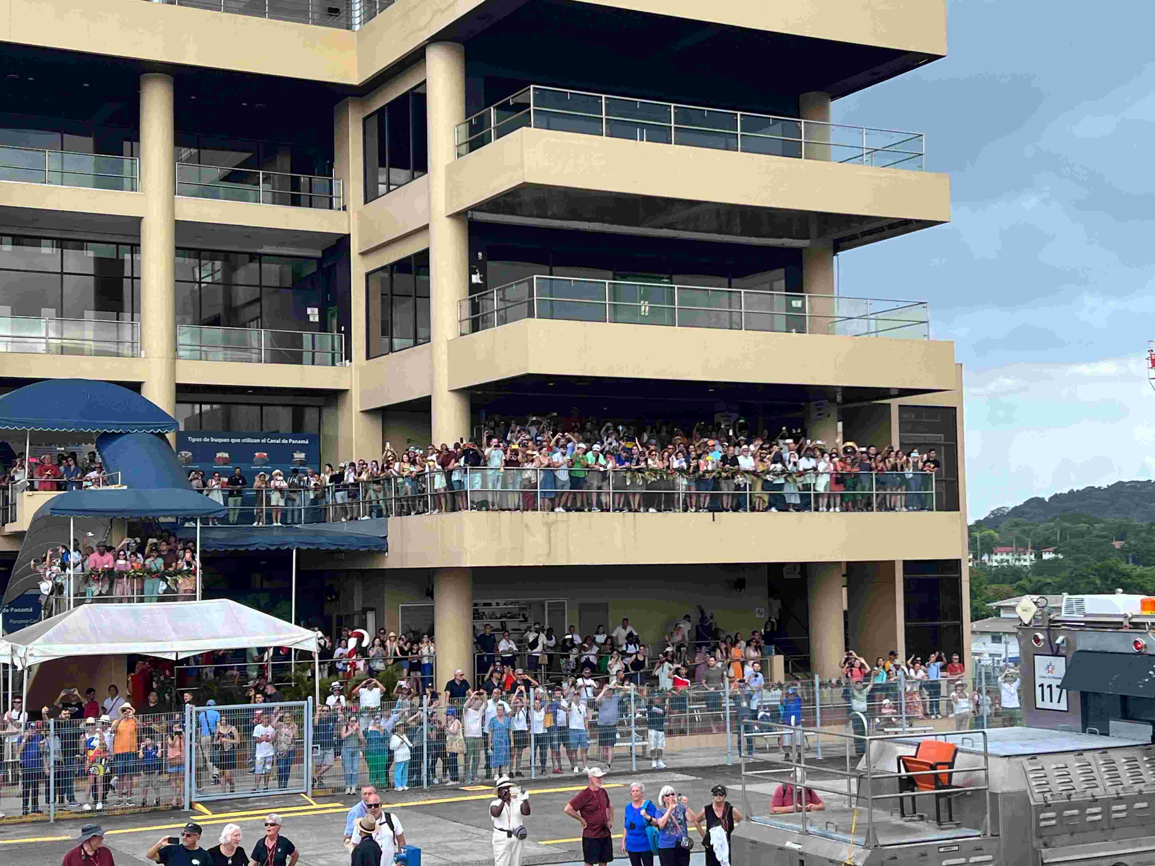 A crowd of visitors in a multi-story tan building cheering for our ship at the Panama Miraflores Lock