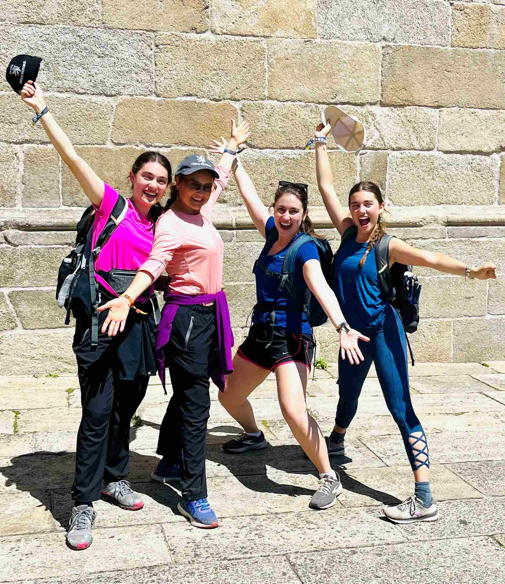 Four young ladies celebrating pose in front of stone wall in Santiago, Spain