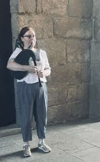 Woman playing bagpipes in front of stone wall in Santigo, Spain