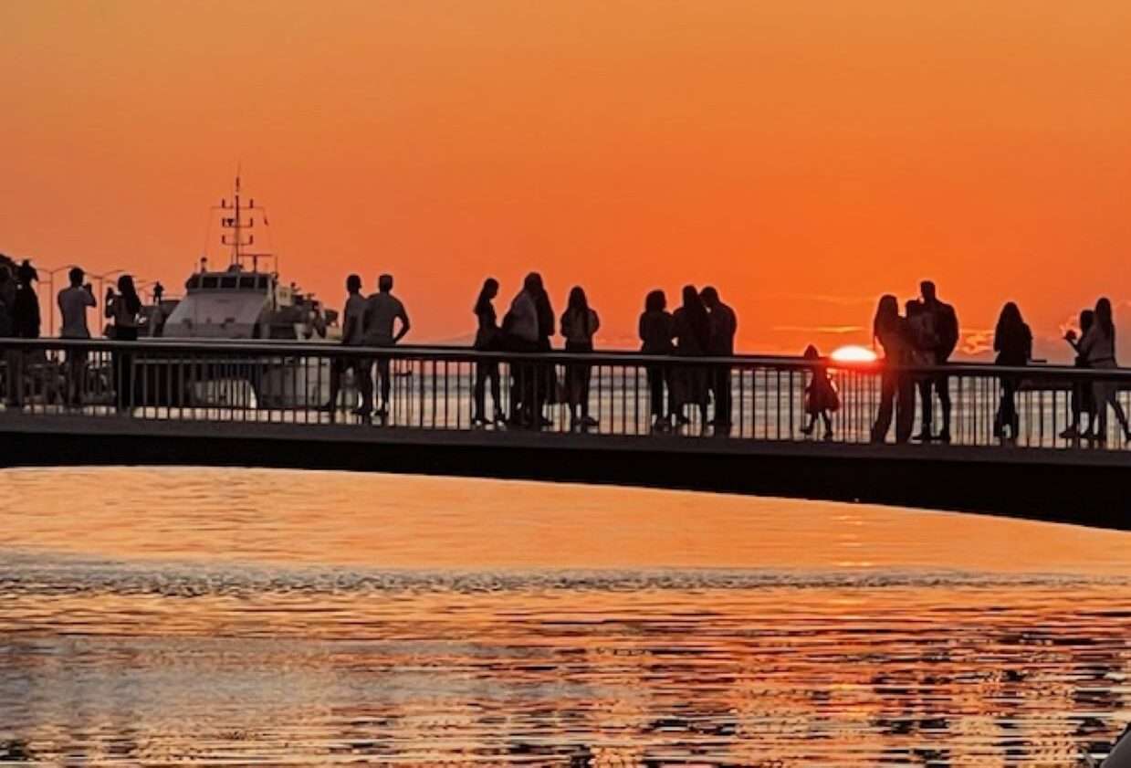 People silhouette against sunset on bridge over water
