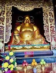 Golden Buddha statue with offerings and flowers.