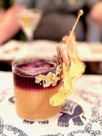 Colorful cocktail with garnish on elephant-patterned tablecloth.