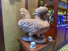 Large carved rooster sculpture in bar setting.