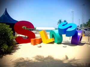 Colorful beach sign on sandy ground.