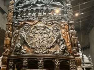 Intricate ship stern with carved lions and coat of arms.