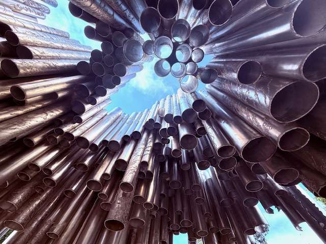 Sculpture of metal pipes with sky view above.