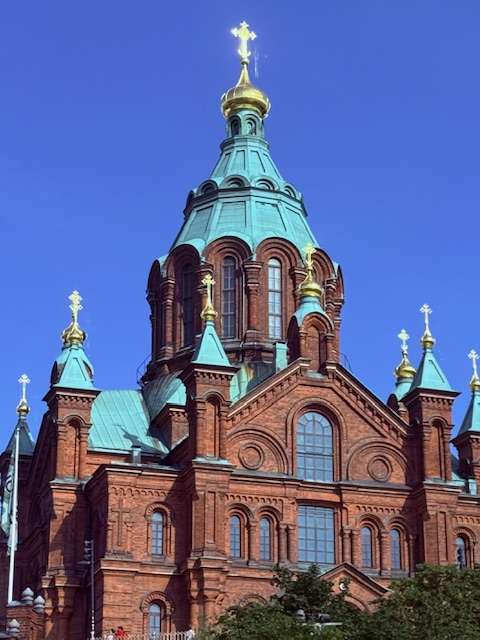 Red brick cathedral with green domes and crosses.