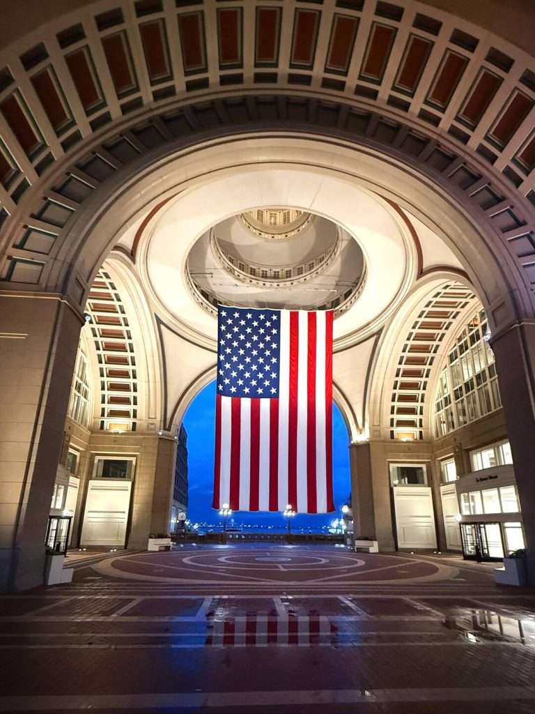 Large American flag under monumental archway.