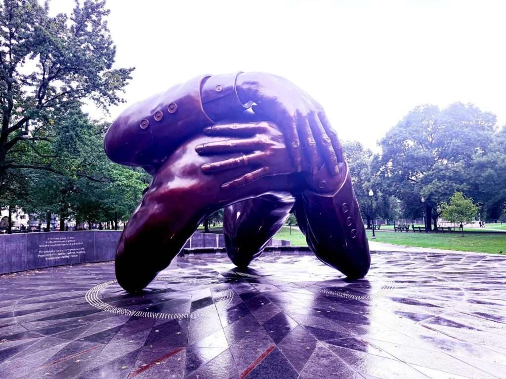 Large abstract sculpture of clasping hands in park.