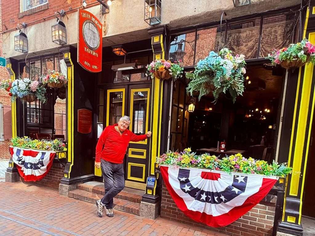 Man outside Green Dragon Tavern with patriotic decor.