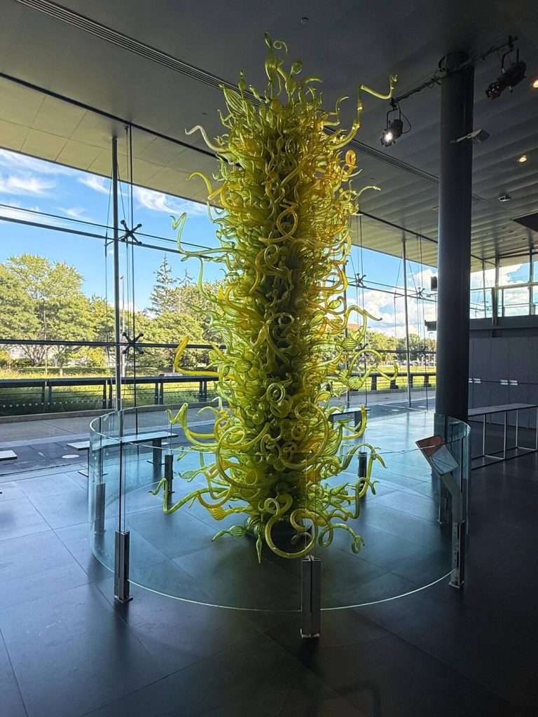 Tall yellow glass sculpture inside museum.
