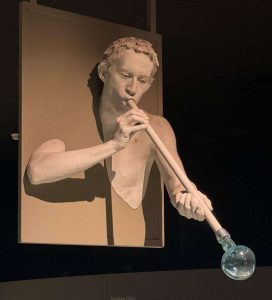 Glassblowing statue above glass display cases.