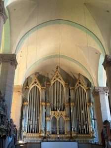 Ornate church pipe organ under vaulted ceiling.