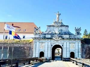 Historic fortress entrance with flags, sunny day.