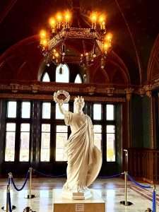 Marble statue under ornate chandelier in historic building.
