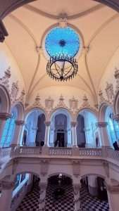 Elegant hall with stained glass dome and chandelier.