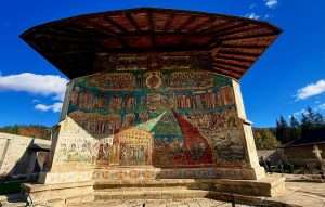 Vivid frescoes on monastery wall under clear blue sky.