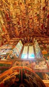 Ornate painted church ceiling with arched window view.