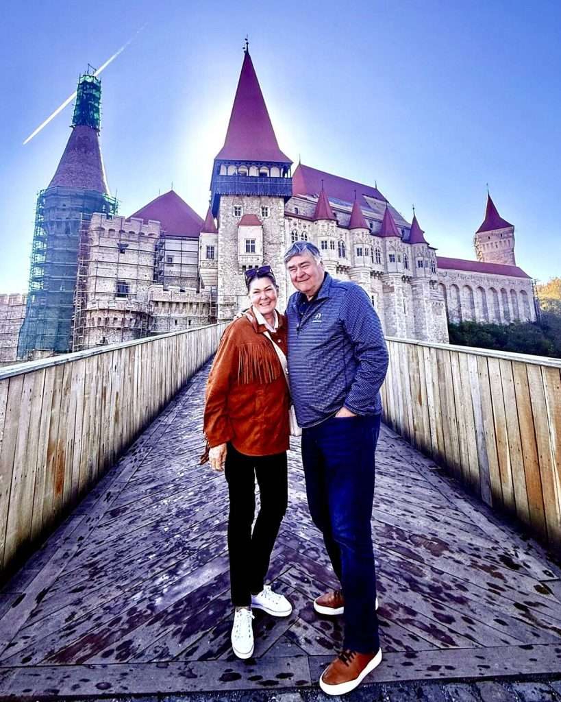 Couple smiling on bridge near large historic castle.
