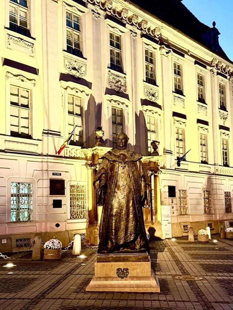 Illuminated statue in front of historic European building.