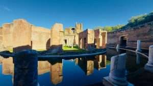 Ancient Roman ruins reflected in water, sunny day.