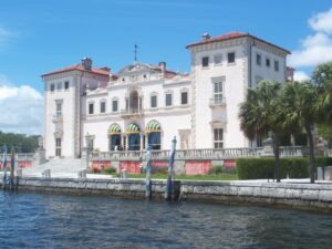 Historic waterfront mansion with palm trees and columns.