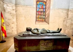 Tomb sculpture with Spanish flag and stained glass window.