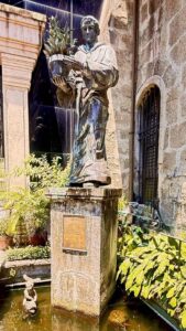 Stone statue holding potted plant in garden setting.
