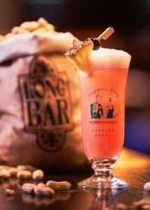 Singapore Sling cocktail with peanuts and pineapple garnish.